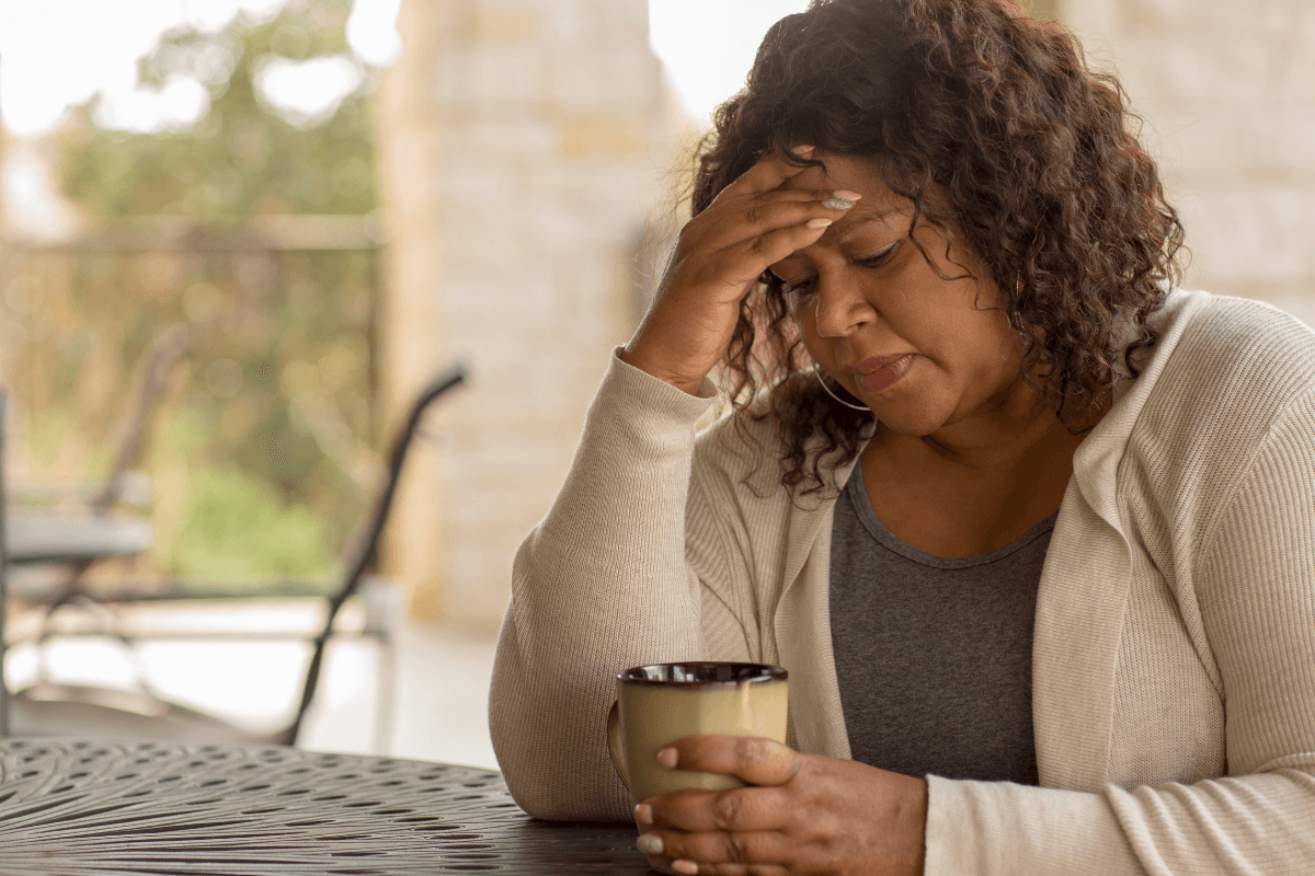 Woman sitting with a mug, holding her forehead